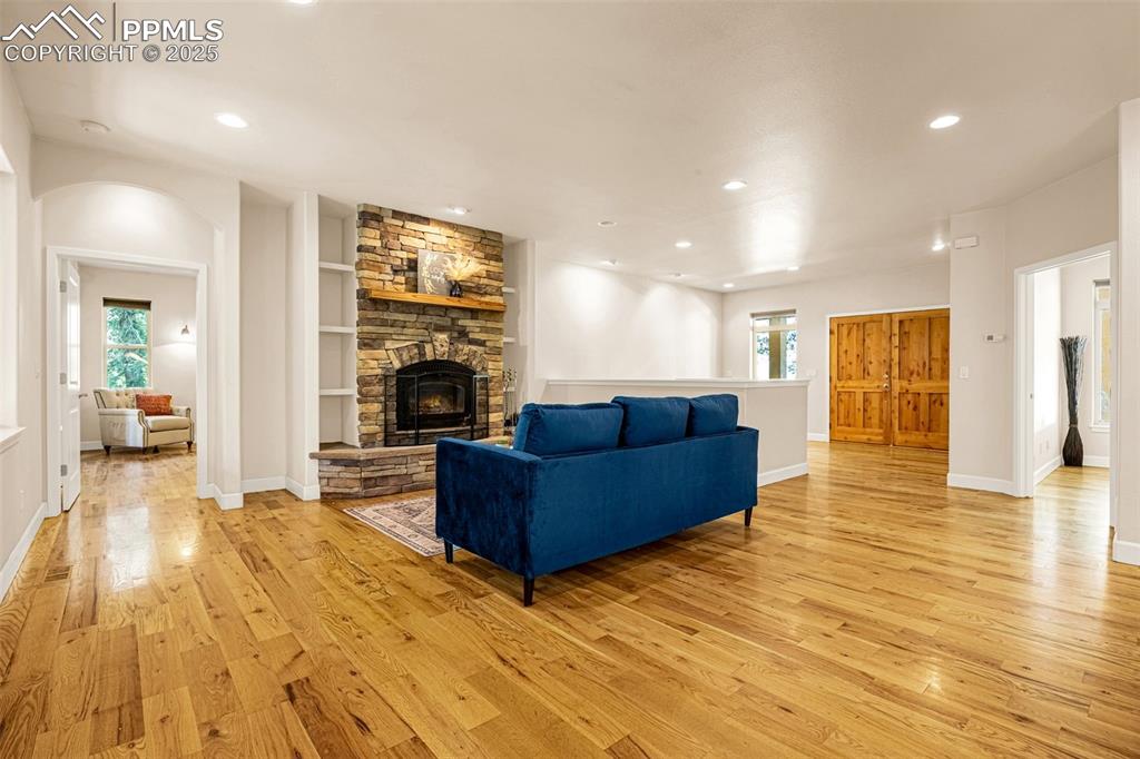 Living area featuring light wood-style flooring, a fireplace, recessed lighting, arched walkways, and baseboards