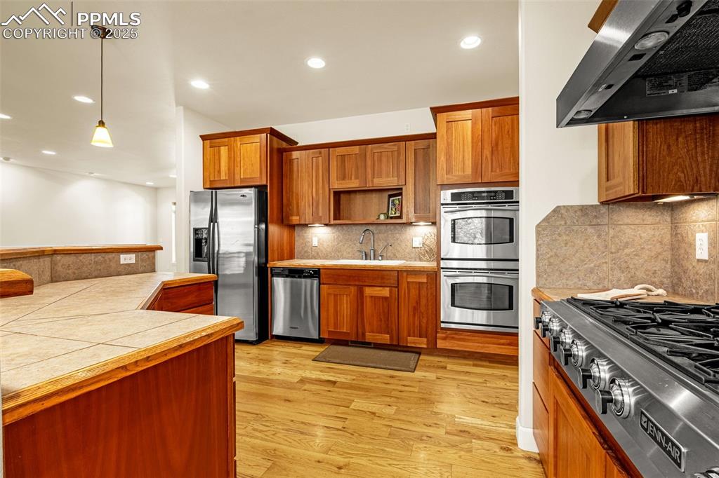 Kitchen with ventilation hood, appliances with stainless steel finishes, a sink, brown cabinets, and open shelves