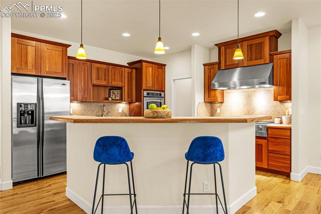 Kitchen featuring stainless steel appliances, under cabinet range hood, a kitchen breakfast bar, light wood finished floors, and recessed lighting