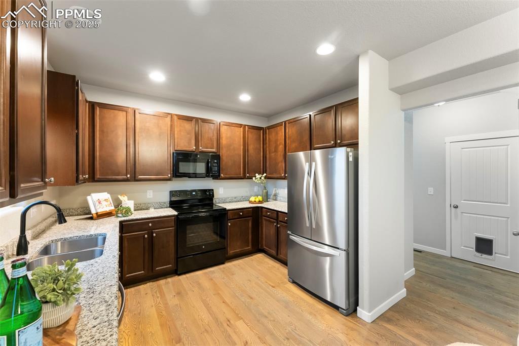 Kitchen featuring black appliances, light stone counters, light wood-style flooring, recessed lighting, and dark brown cabinetry