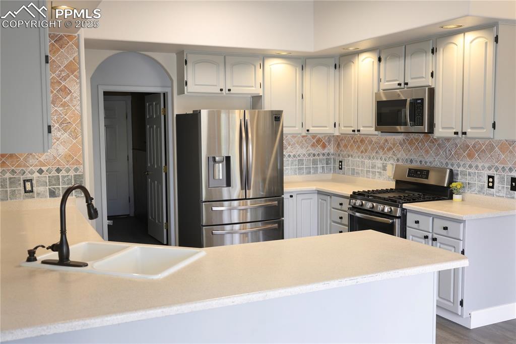 Kitchen with appliances with stainless steel finishes, tasteful backsplash, recessed lighting, light stone counters, and white cabinetry