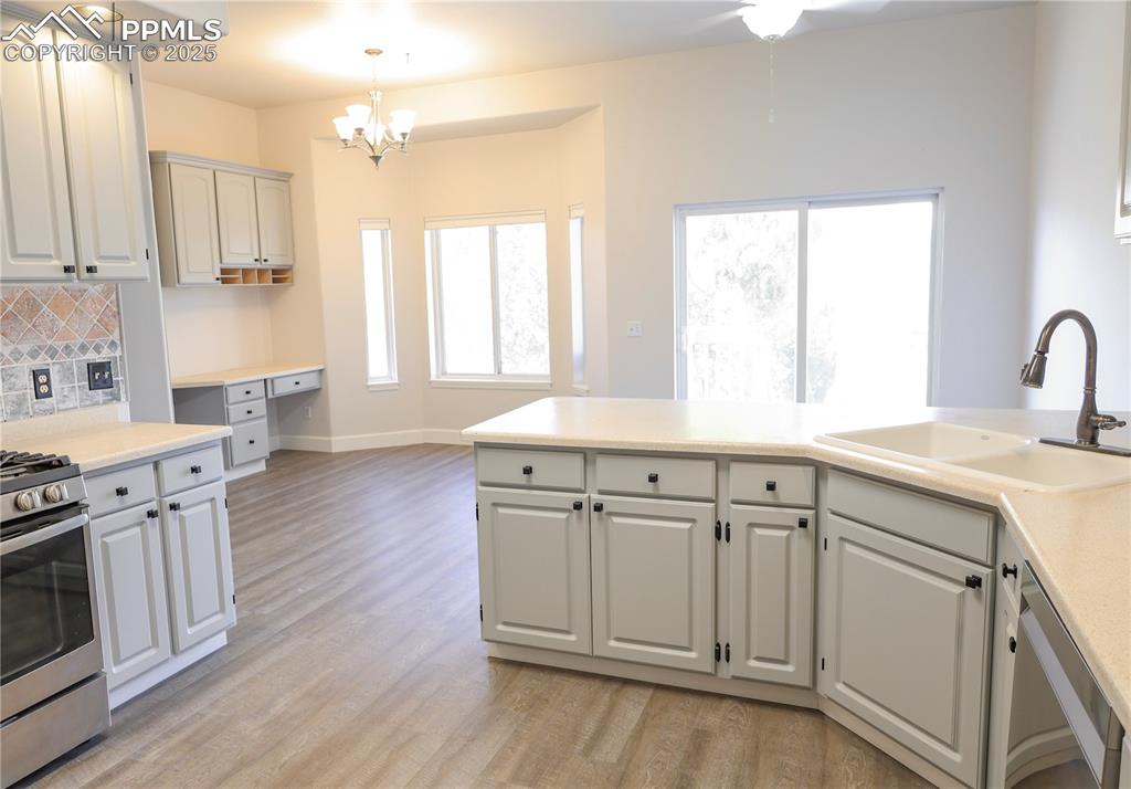 Kitchen featuring decorative backsplash, appliances with stainless steel finishes, light countertops, light wood finished floors, and a chandelier