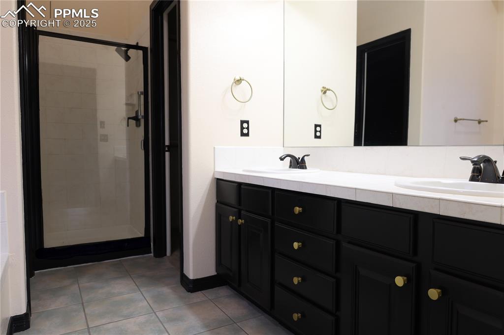 Bathroom featuring tile patterned flooring, double vanity, and a shower stall