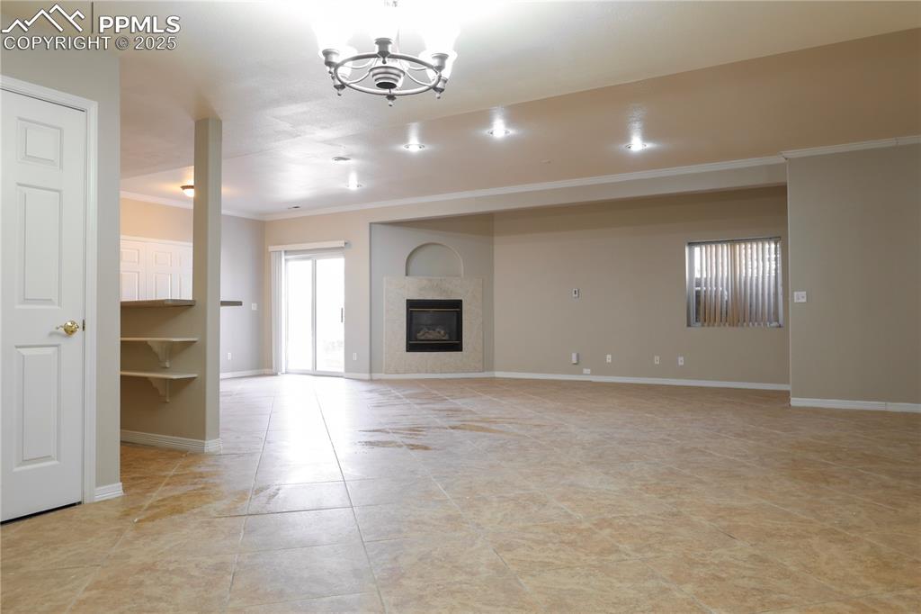 Unfurnished living room with a glass covered fireplace, crown molding, a chandelier, and light tile patterned flooring