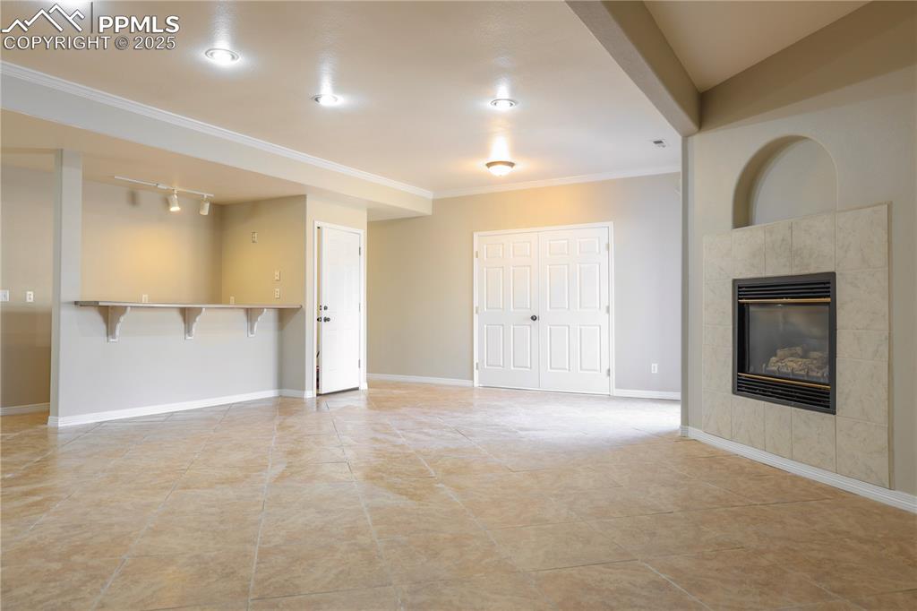 Unfurnished living room with a tile fireplace, light tile patterned floors, ornamental molding, and rail lighting