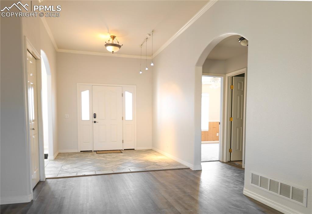 Spacious foyer entrance with crown molding, arched walkways, and wood finished floors
