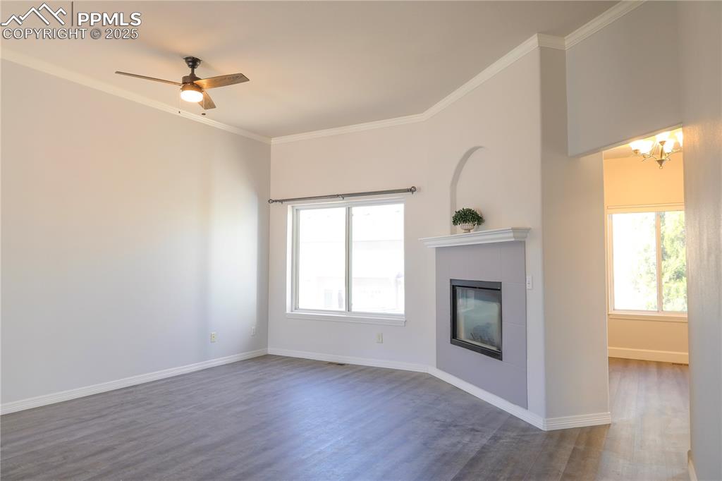 Unfurnished living room featuring ornamental molding, dark wood-style flooring, a tiled fireplace, a ceiling fan, and a chandelier