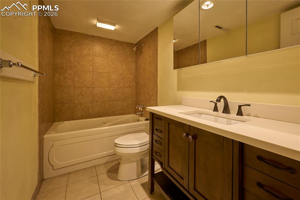 Full bath featuring tile floors, toilet, jetted bathtub / shower combination, and vanity