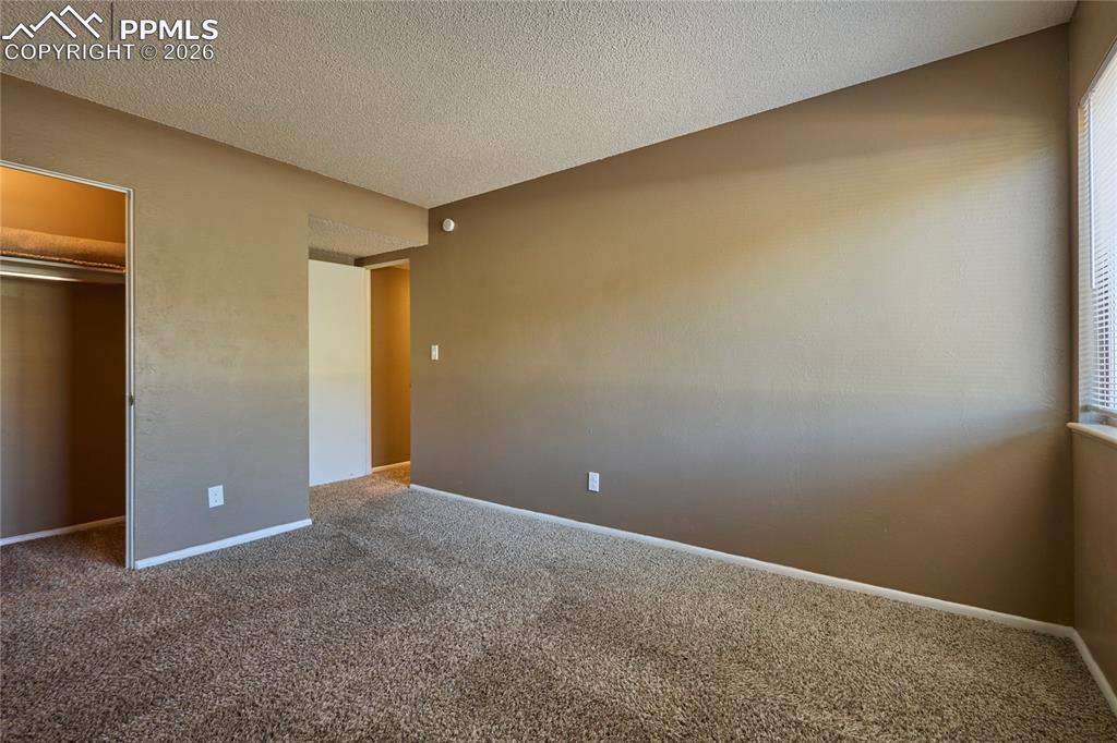Unfurnished bedroom with a spacious closet, carpet floors, a closet, baseboards, and a textured ceiling