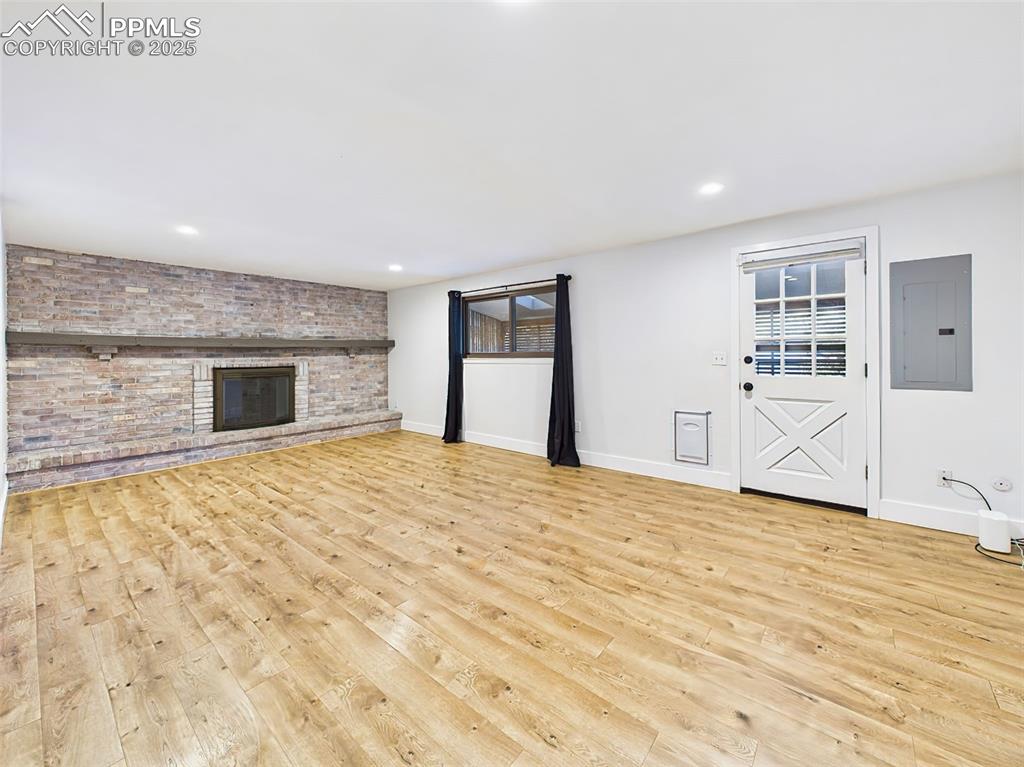 Spacious and versatile lower-level room with wide-plank flooring, brick fireplace, and natural light—ideal for a media or game room.