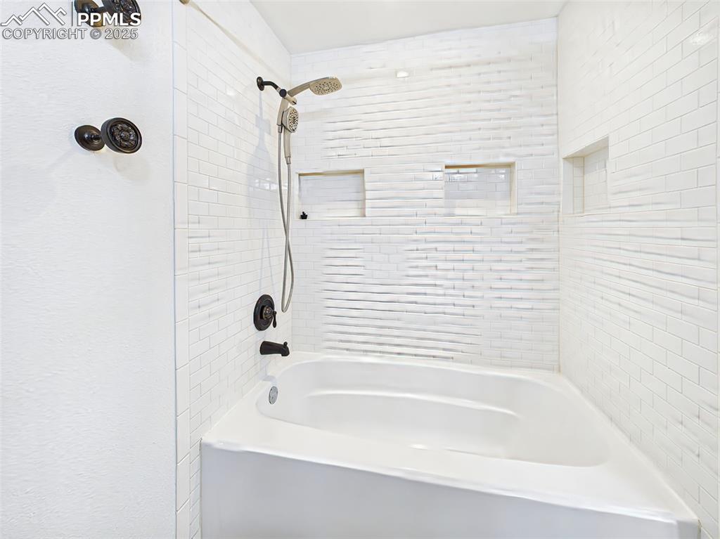 Stylishly updated bath and shower combo with crisp white tilework, built-in niches, and matte black fixtures, including body jets and a handheld sprayer.
