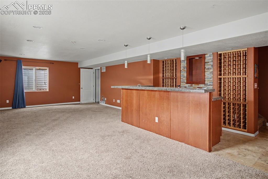 Kitchen featuring light colored carpet, hanging light fixtures, dark stone countertops, open floor plan, and wood finish cabinetry