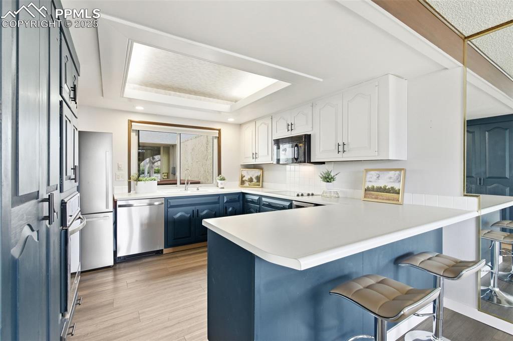 Kitchen featuring blue cabinets, white cabinetry, light countertops, a tray ceiling, and a peninsula