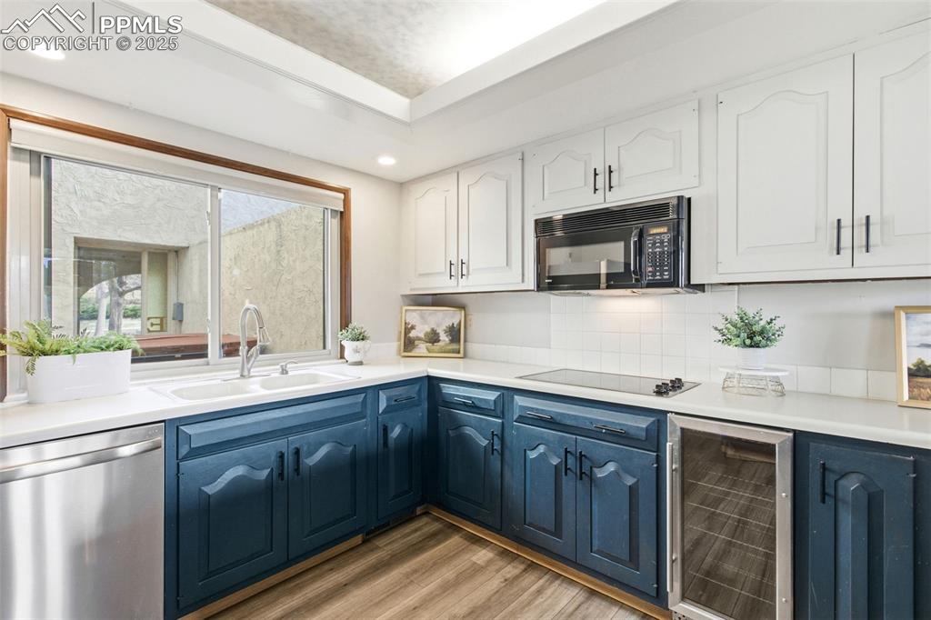 Kitchen featuring beverage cooler, black appliances, white cabinets, blue cabinets, and light wood-style flooring