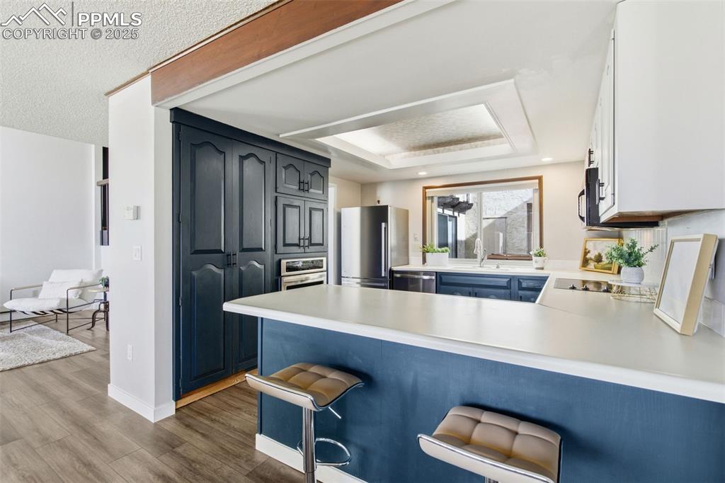 Kitchen with a breakfast bar area, light countertops, appliances with stainless steel finishes, a tray ceiling, and a peninsula