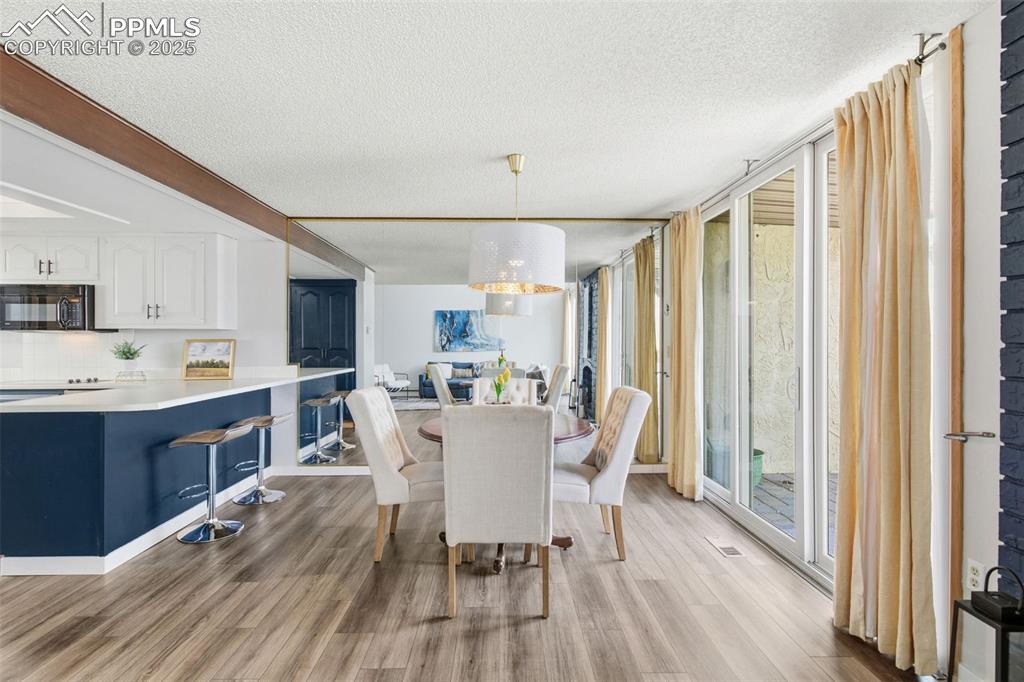 Dining space featuring light wood-style flooring, a wall of windows, a textured ceiling, and beamed ceiling