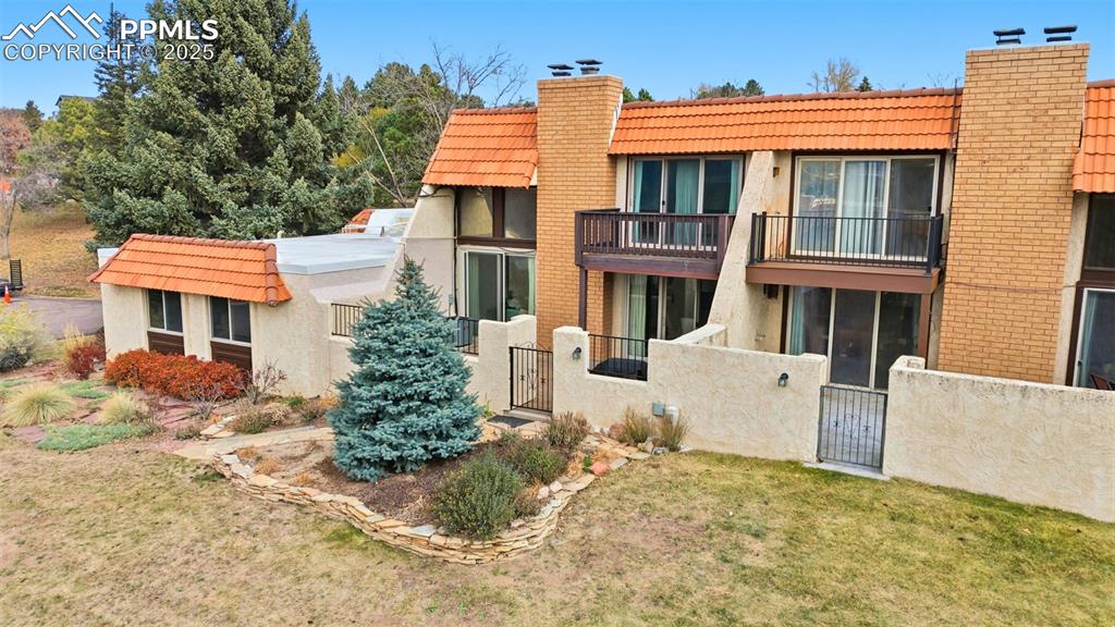 Rear view of house with a chimney, a tiled roof, stucco siding, a balcony, and a gate
