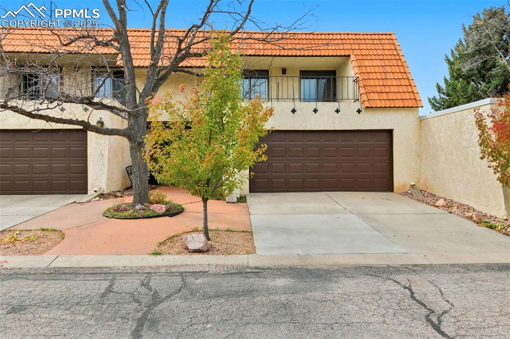 View of front of house featuring stucco siding, a balcony, driveway, and a tiled roof
