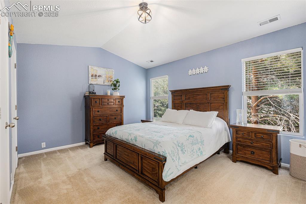Bedroom featuring light colored carpet, vaulted ceiling with vaulted ceilings with updated lighting, and ensuite bathroom