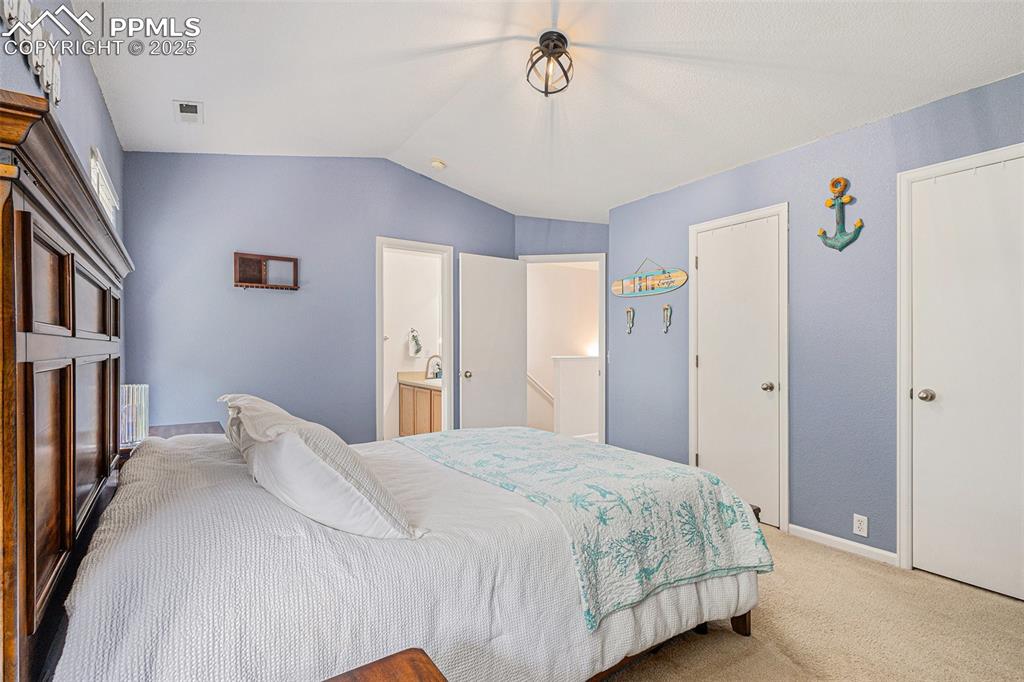Bedroom featuring light colored carpet, vaulted ceiling with vaulted ceilings with updated lighting, and ensuite bathroom