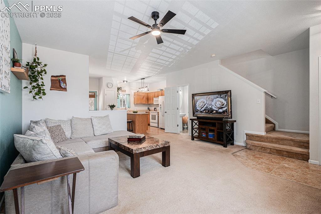 Living area with light carpet, stairway, and updated lighting and ceiling fan