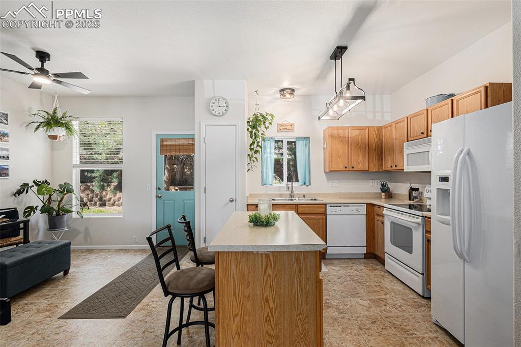 Kitchen featuring white appliances, updated lighting, a kitchen island, a kitchen breakfast bar, and open floor plan with updated lighting and ceiling fan