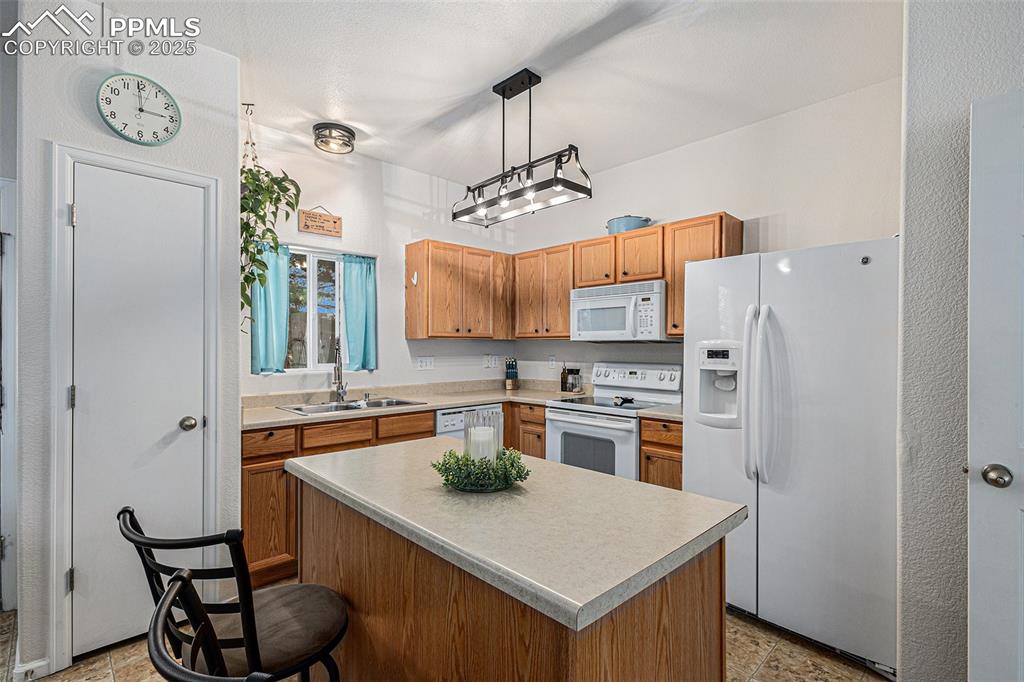 Kitchen featuring white appliances, updated lighting, a kitchen island, a kitchen breakfast bar, and open floor plan with updated lighting