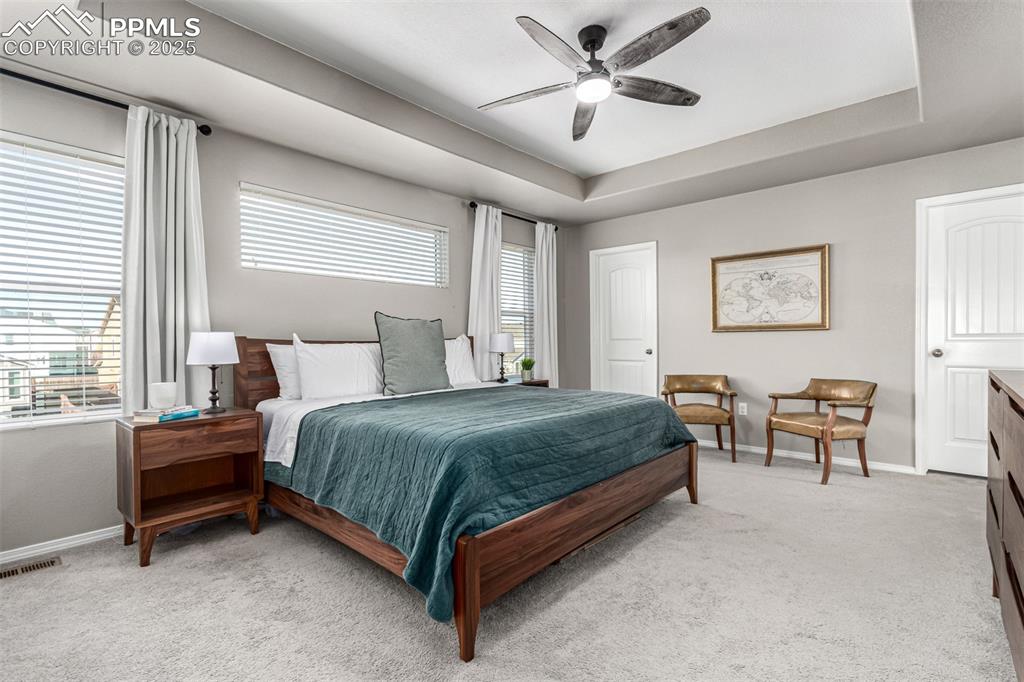 Bedroom with a tray ceiling, light carpet, and ceiling fan