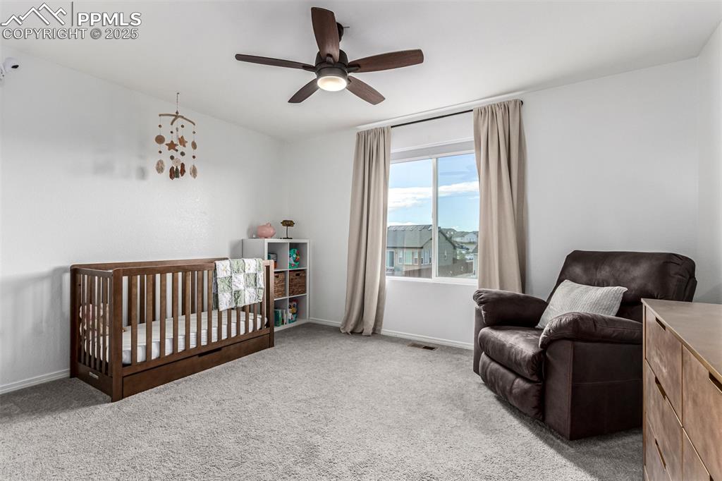 Bedroom with a crib, carpet flooring, and ceiling fan