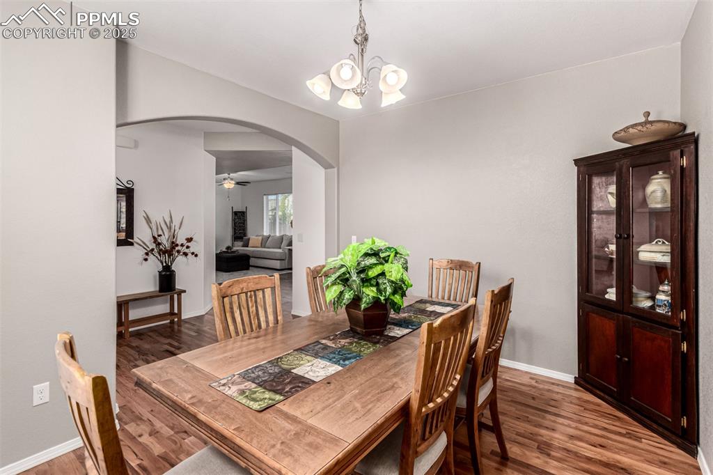 Dining area with arched walkways, dark wood-style flooring, a chandelier, and ceiling fan