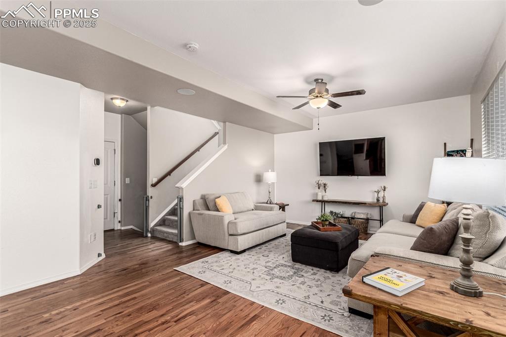 Living area with stairway, dark wood-type flooring, and a ceiling fan