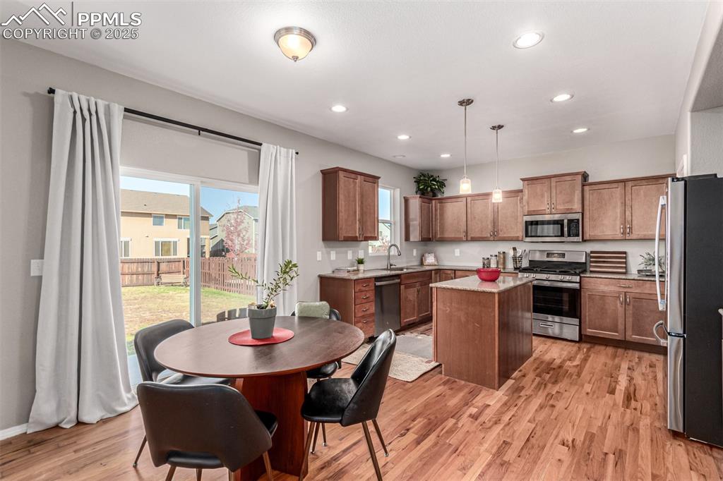Kitchen with hanging light fixtures, a center island, appliances with stainless steel finishes, recessed lighting, and light wood-style flooring