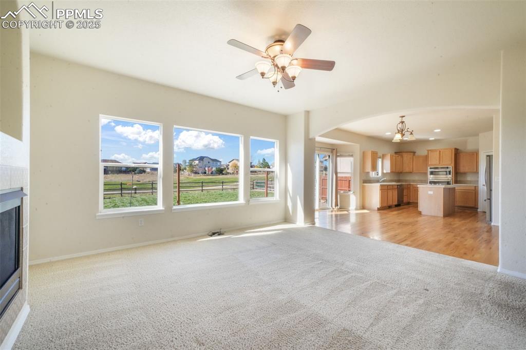 Unfurnished living room featuring light colored carpet, arched walkways, a chandelier, a fireplace, and ceiling fan