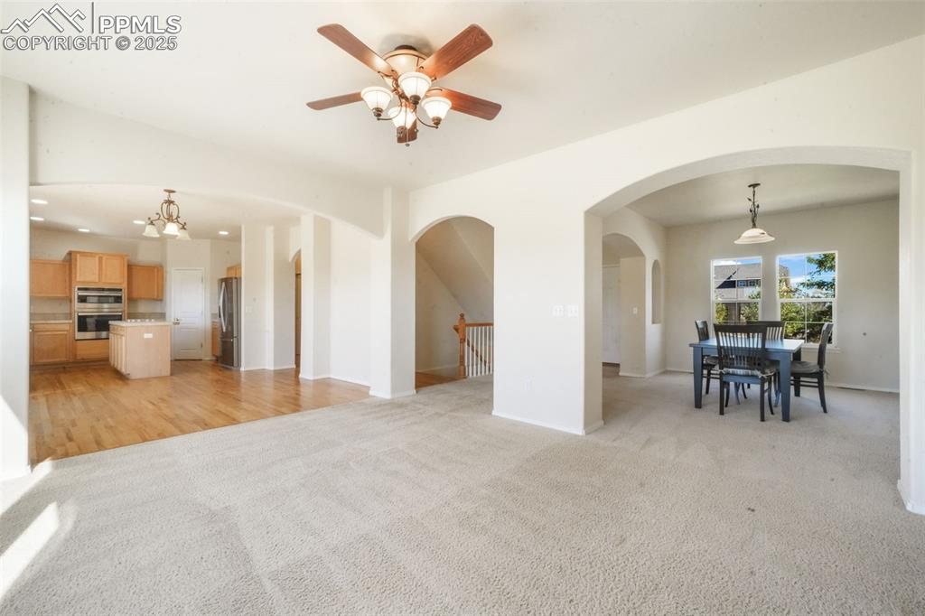 Unfurnished living room with light colored carpet, a ceiling fan, a chandelier, and arched walkways