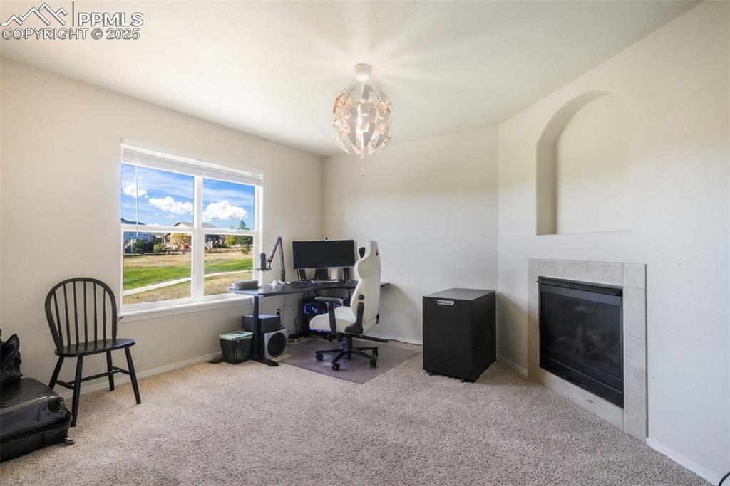 Office space with a tiled fireplace, light colored carpet, and a chandelier