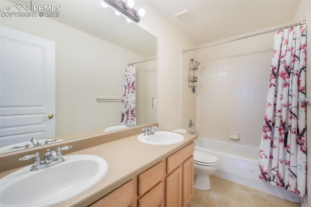 Full bath featuring double vanity, shower / bathtub combination with curtain, and light tile patterned floors