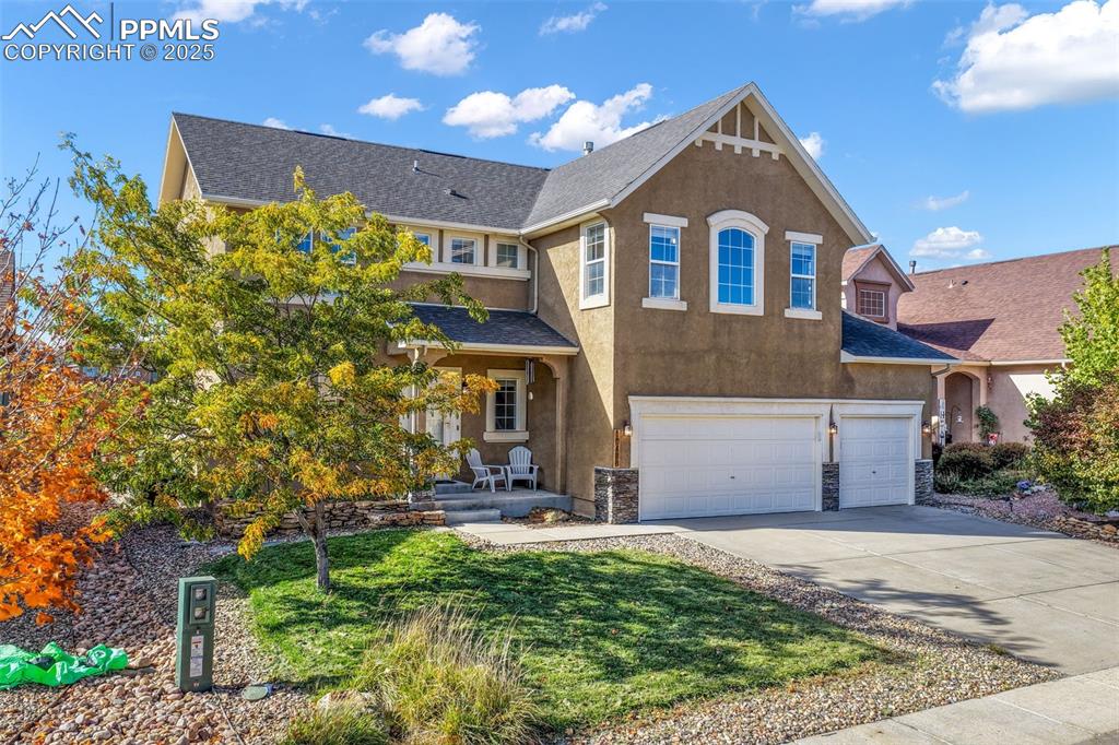 View of front facade featuring a front yard, concrete driveway, a garage, a shingled roof, and stucco siding