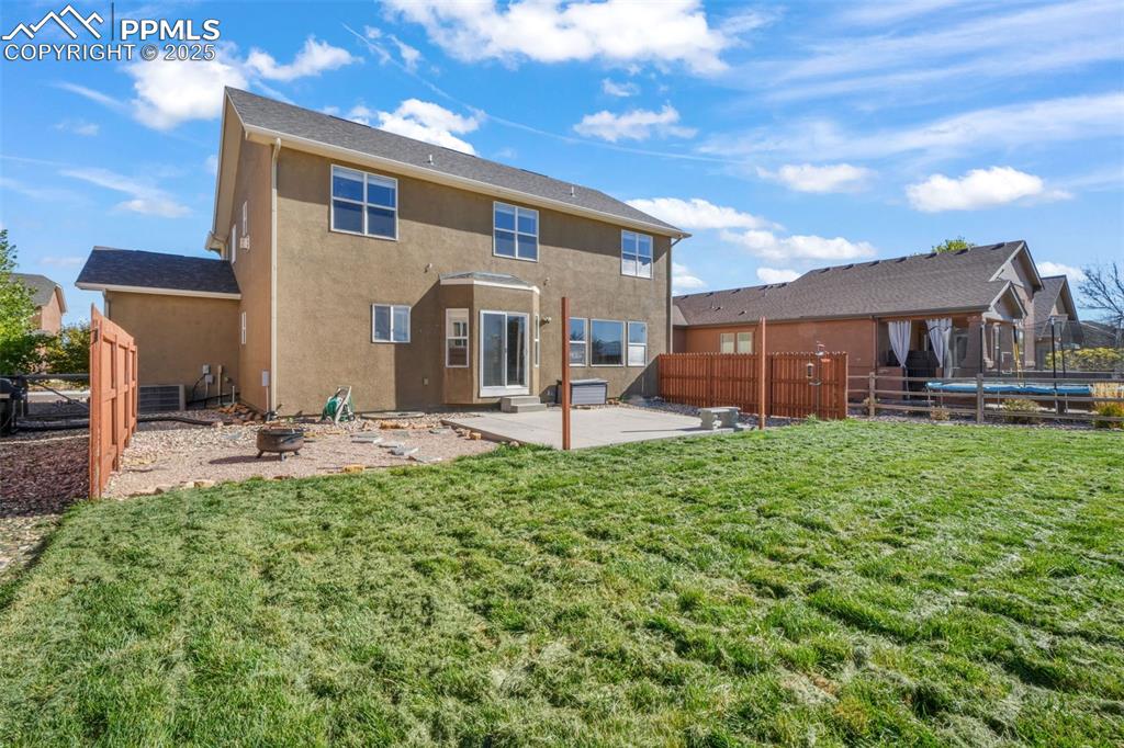 Rear view of property featuring a patio area, stucco siding, a fenced backyard, a trampoline, and an outdoor fire pit