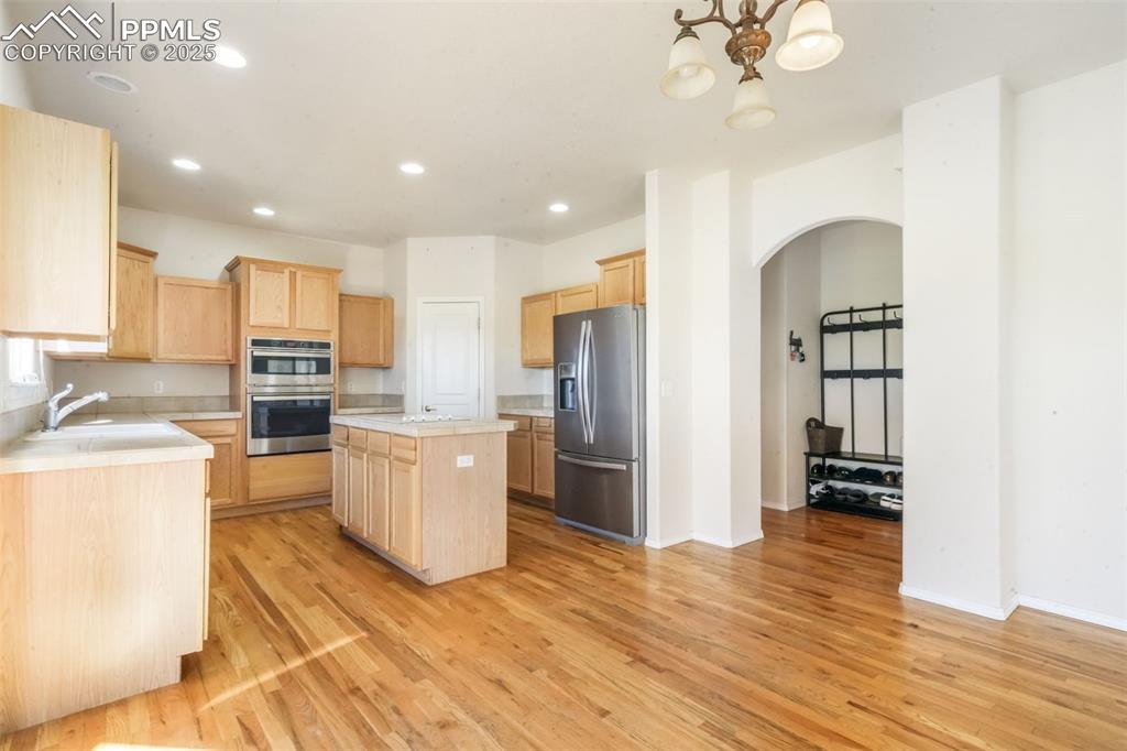Kitchen featuring light brown cabinets, arched walkways, a center island, appliances with stainless steel finishes, and light wood-type flooring