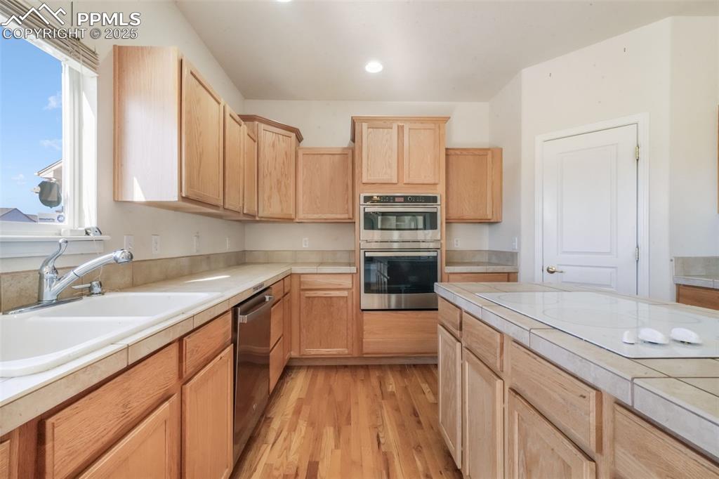 Kitchen with tile countertops, light brown cabinetry, stainless steel appliances, light wood-style flooring, and recessed lighting