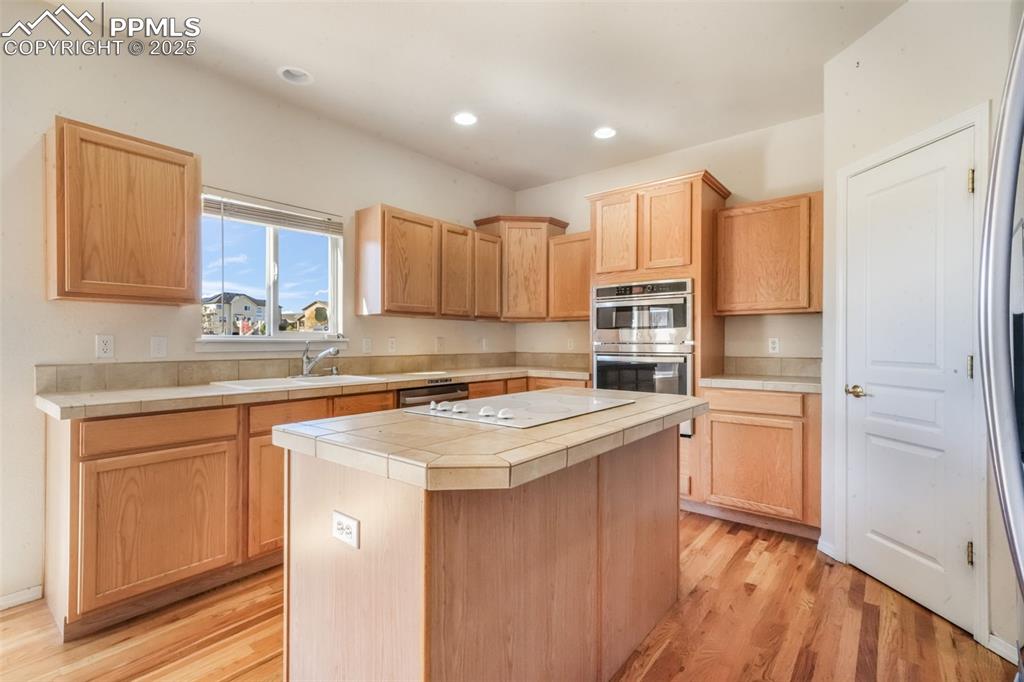 Kitchen featuring tile countertops, a center island, light wood-style floors, light brown cabinets, and recessed lighting