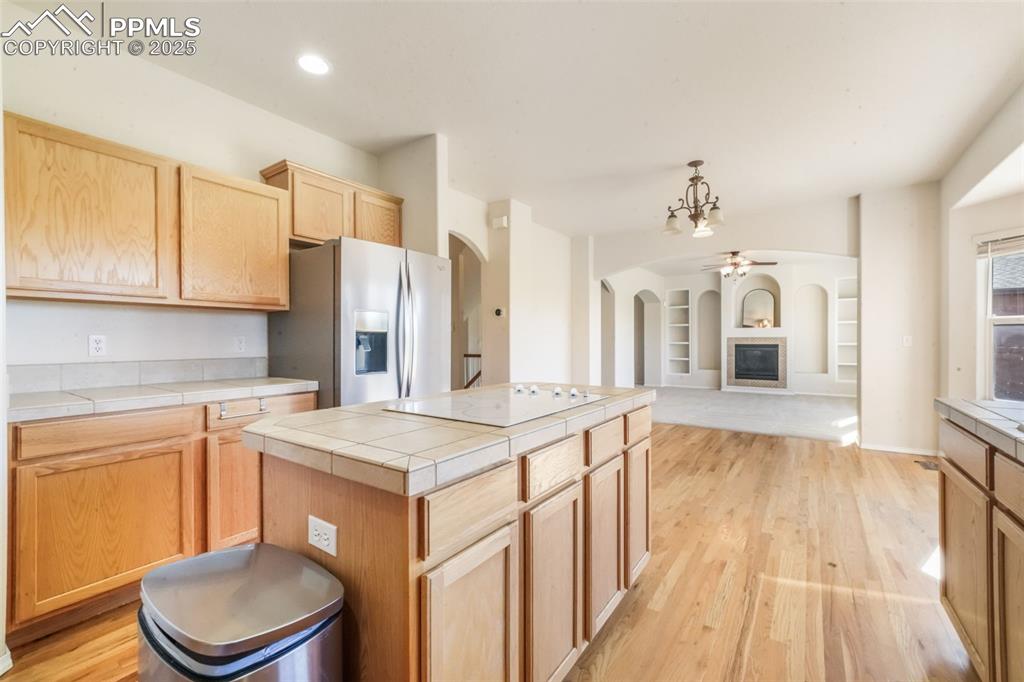 Kitchen featuring light brown cabinets, a glass covered fireplace, light wood-type flooring, stainless steel fridge, and recessed lighting