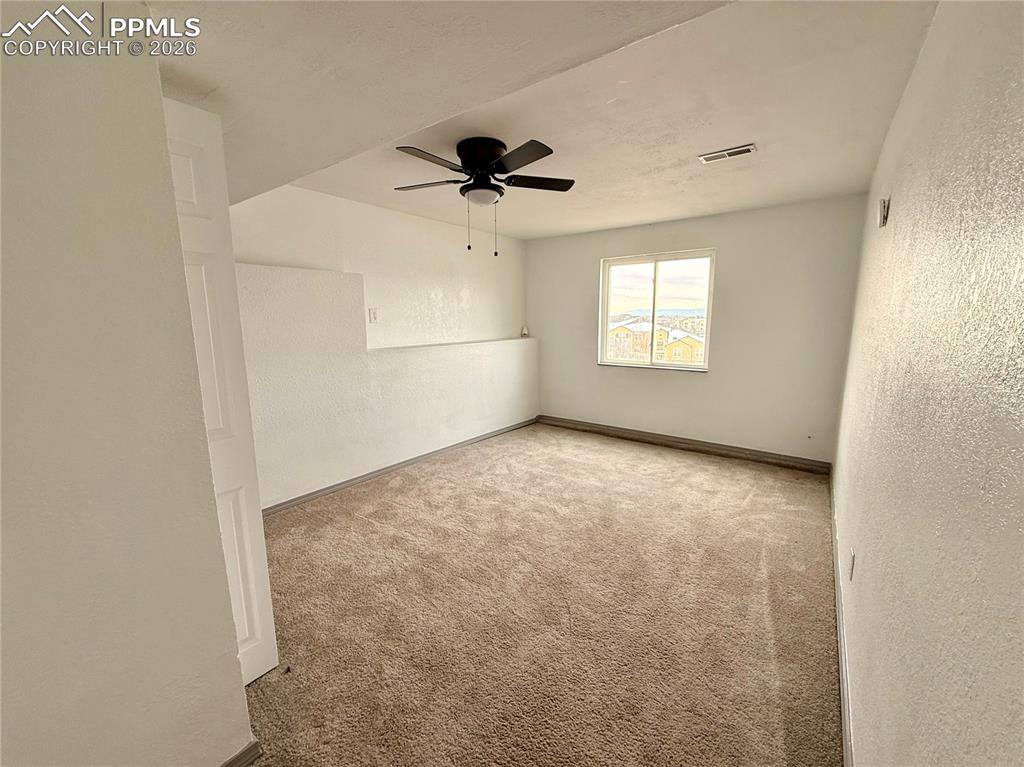 Carpeted empty room featuring a textured wall and a ceiling fan
