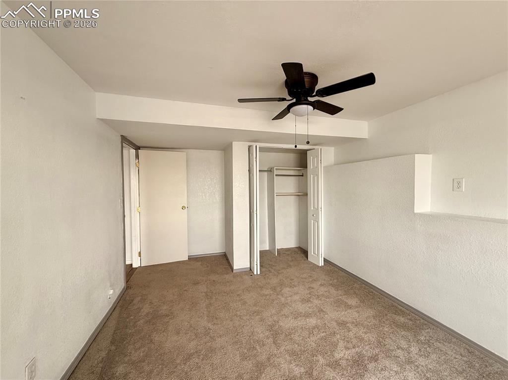 Unfurnished bedroom featuring a textured wall, a ceiling fan, carpet, and a closet