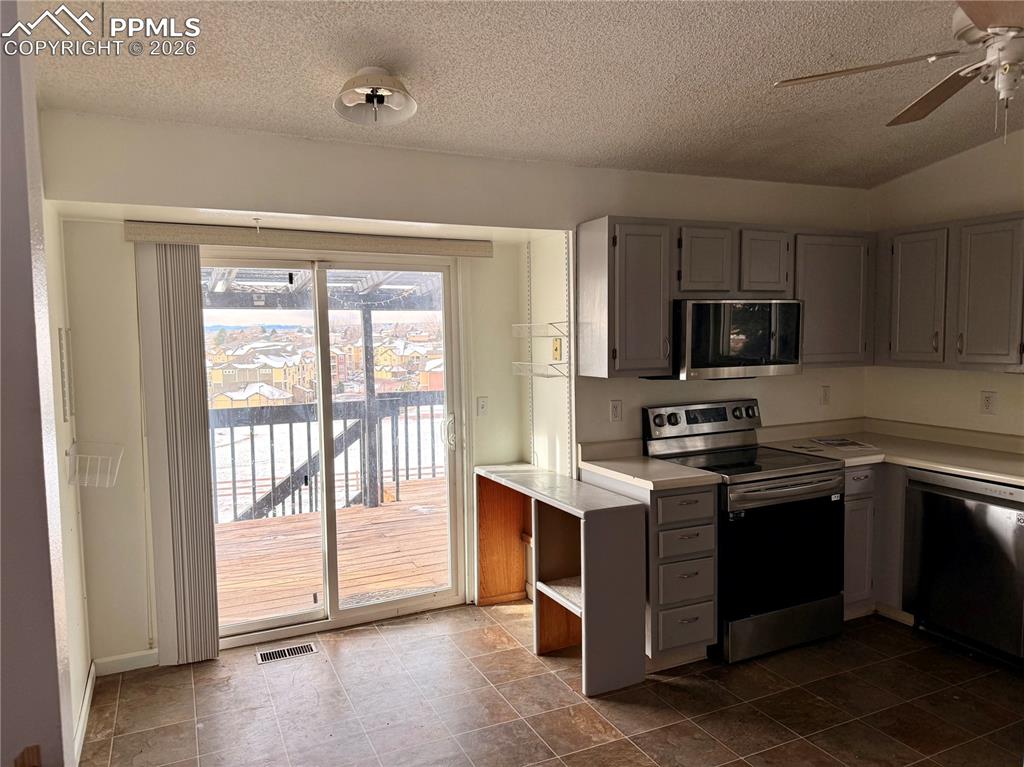 Kitchen featuring stainless steel appliances, light countertops, gray cabinetry, a ceiling fan, and a textured ceiling