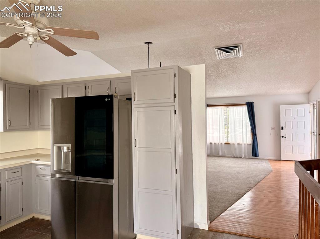 Kitchen featuring stainless steel fridge with ice dispenser, a textured ceiling, light countertops, dark wood-style floors, and ceiling fan