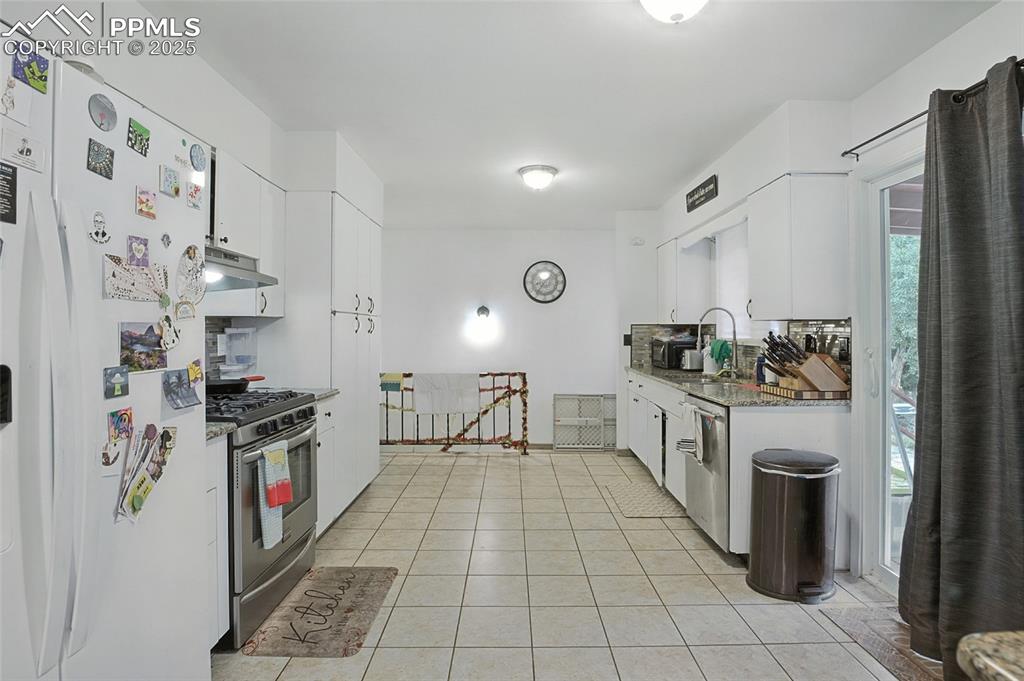 Kitchen with appliances with stainless steel finishes, white cabinetry, light stone counters, light tile patterned flooring, and under cabinet range hood