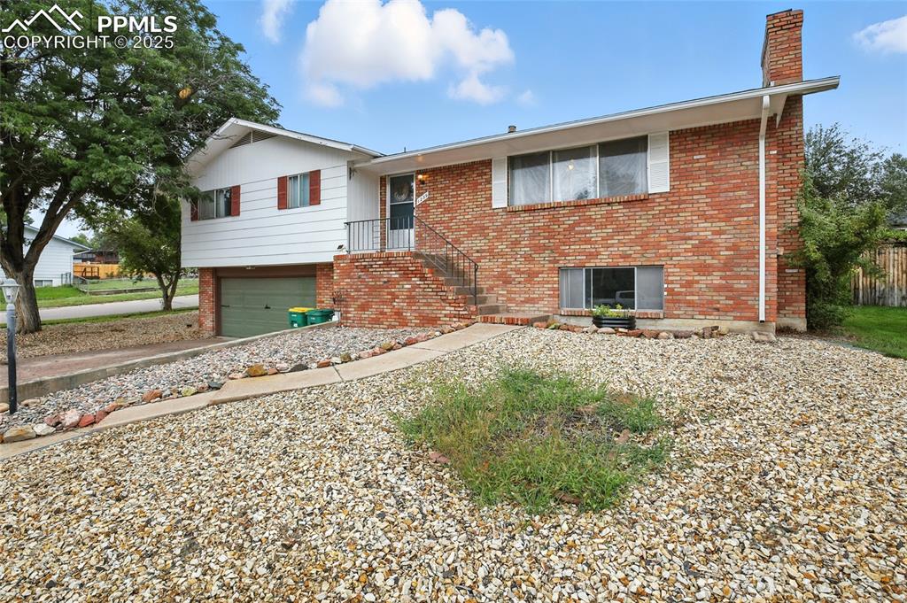 View of front of property with brick siding, a garage, a chimney, and driveway