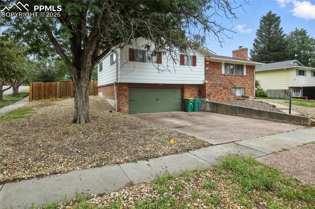 View of front of home featuring concrete driveway, brick siding, a garage, and a chimney