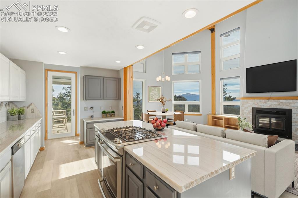 Virtually Staged - Kitchen featuring stainless steel appliances, light stone countertops, light wood finished floors, gray cabinets, and a glass covered fireplace